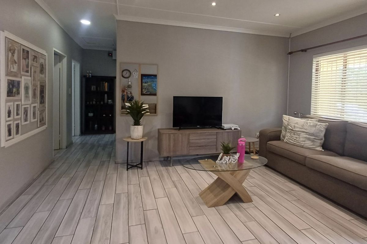 A well-maintained living room featuring modern light-toned tiled flooring, recessed downlighting, and venetian blinds, creating a bright and comfortable living space.