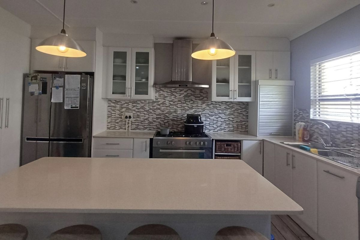 Modern kitchen featuring a central island, mosaic tile backsplash, stainless steel appliances, ample cabinetry, and pendant lighting, creating a functional and bright workspace.