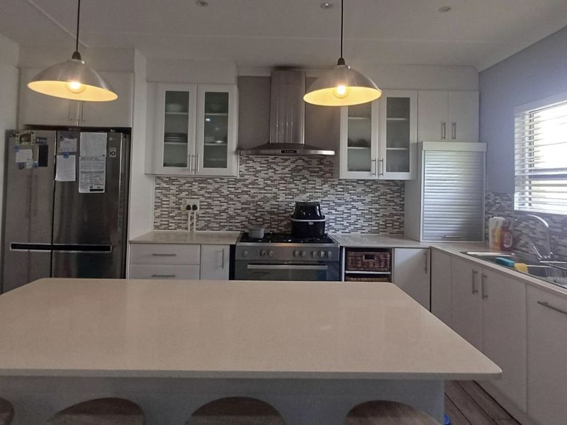 Modern kitchen featuring a central island, mosaic tile backsplash, stainless steel appliances, ample cabinetry, and pendant lighting, creating a functional and bright workspace.