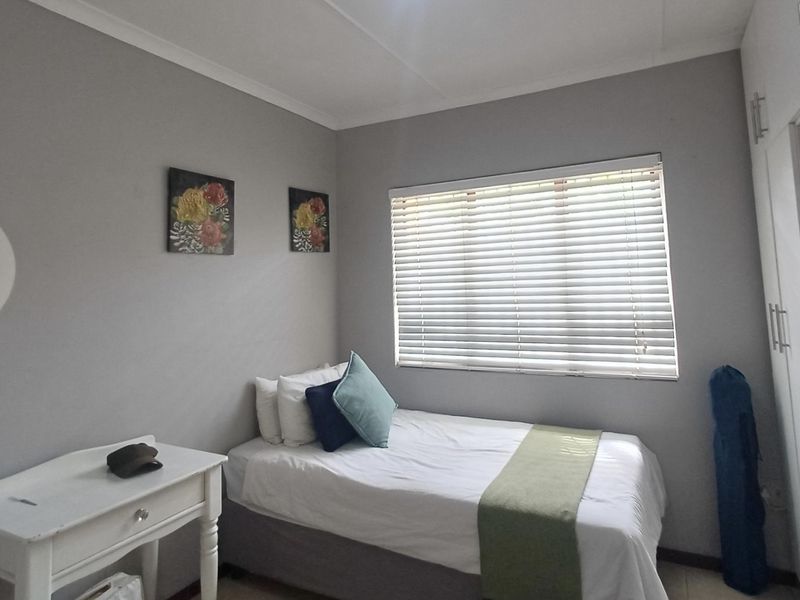 A functional bedroom featuring built-in cupboards and venetian blinds, providing a neutral and practical living space.
