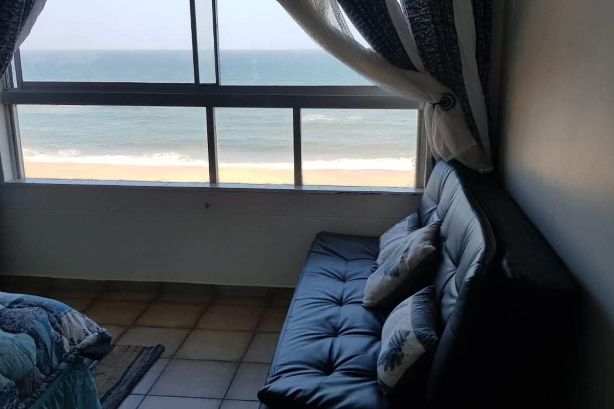 A bedroom featuring tiled flooring and a large sliding window offering direct ocean and beach views.