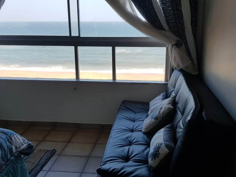 A bedroom featuring tiled flooring and a large sliding window offering direct ocean and beach views.