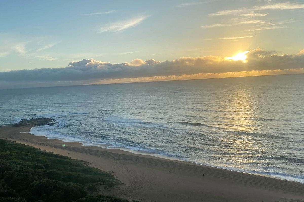 A scenic elevated view of the coastline featuring a sandy beach and ocean at sunrise.