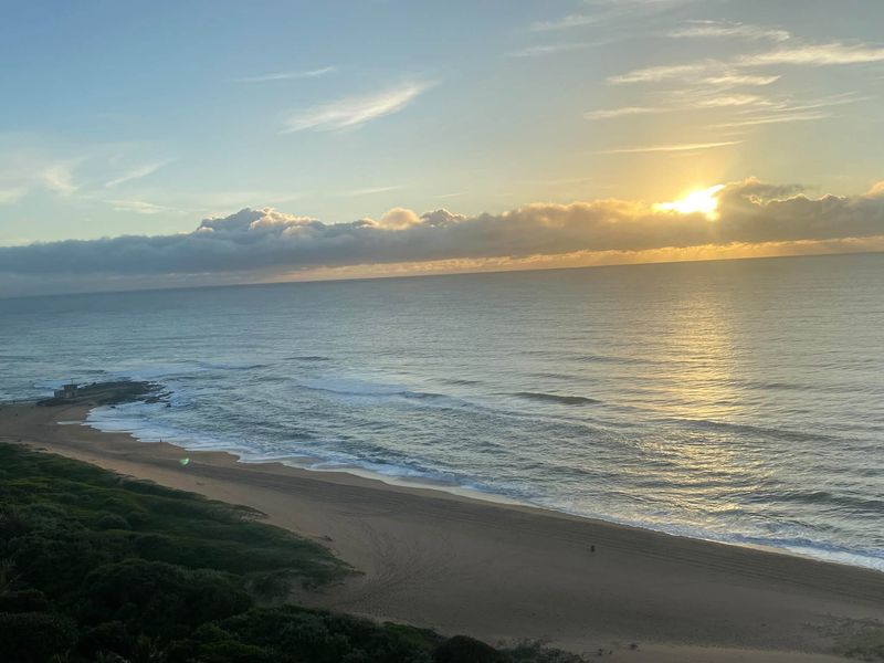 A scenic elevated view of the coastline featuring a sandy beach and ocean at sunrise.