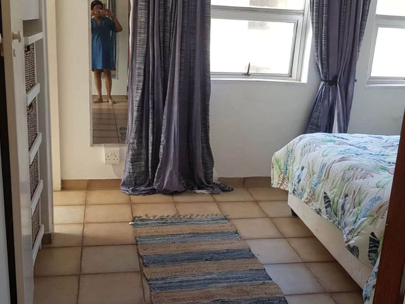 A bedroom featuring tiled flooring and aluminium window frames, offering a functional space with built-in storage options.