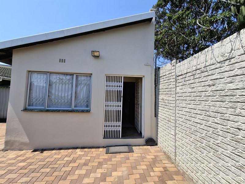 Rear exterior view of the cottage featuring a paved patio area, security gate, and a brick boundary wall.