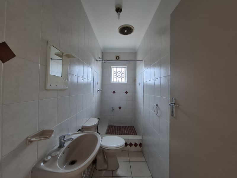 A compact bathroom featuring a pedestal basin, toilet, and a tiled shower cubicle with a security grille on the window.