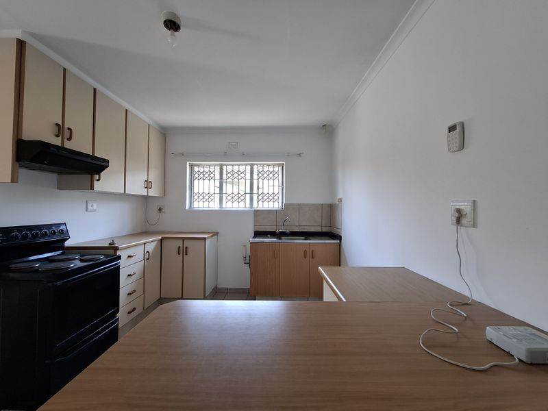A functional kitchen featuring built-in cabinetry, laminate countertops, a stainless steel sink, and an extractor fan, with security bars installed on the window.