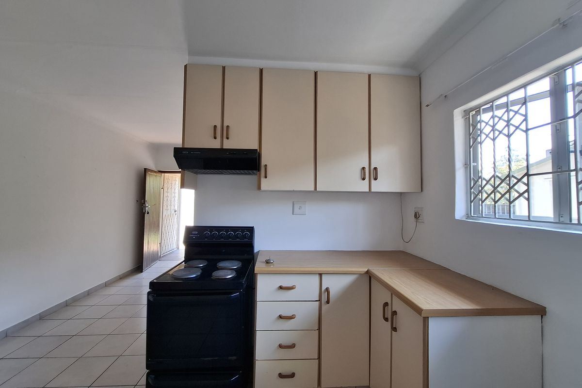 A functional kitchen featuring built-in cabinetry, laminate countertops, a freestanding stove with extractor fan, and tiled flooring, offering a clean and practical workspace.