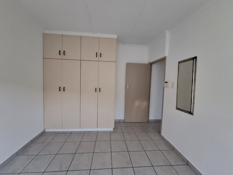 A clean, empty bedroom featuring neutral tiled flooring and ample built-in cupboard storage space.