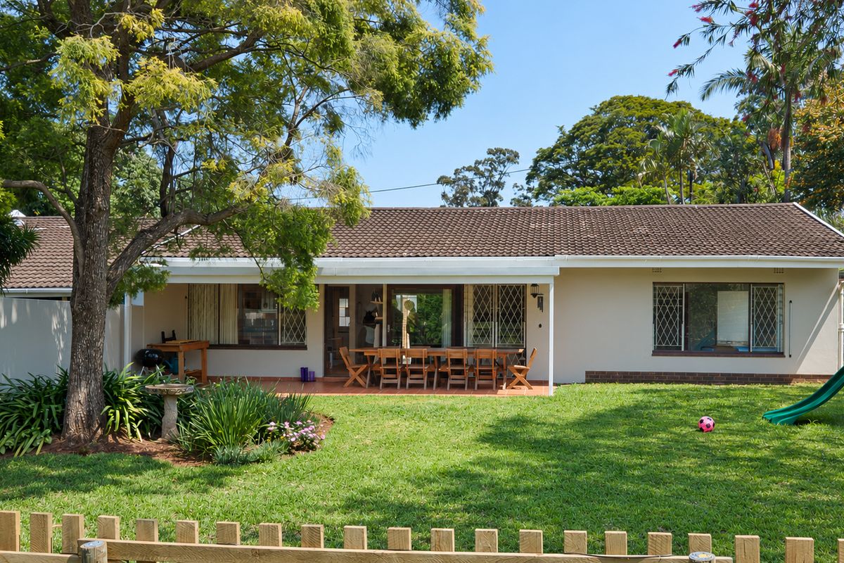 Rear view of the townhouse featuring a covered patio, tiled roof, and a well-maintained garden with mature trees and a lawn.