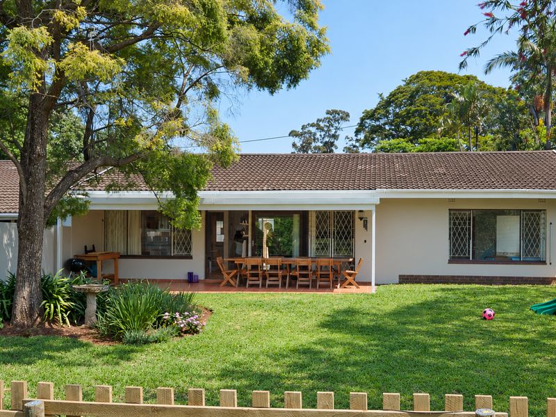 Rear view of the townhouse featuring a covered patio, tiled roof, and a well-maintained garden with mature trees and a lawn.