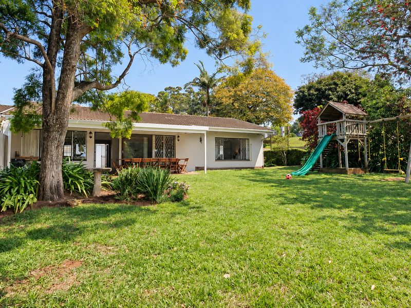Spacious rear garden featuring a well-maintained lawn, mature trees, and a covered patio area accessible through sliding glass doors.