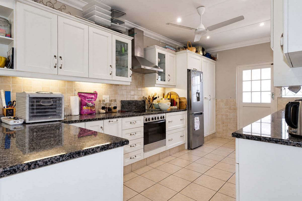 A well-maintained kitchen featuring white cabinetry, granite countertops, tiled backsplash, and built-in oven with stainless steel extractor fan.