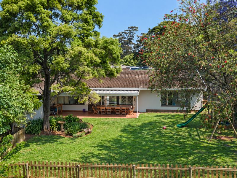 Rear view of the townhouse featuring a spacious lawn, mature trees, and a covered patio area perfect for outdoor entertaining.