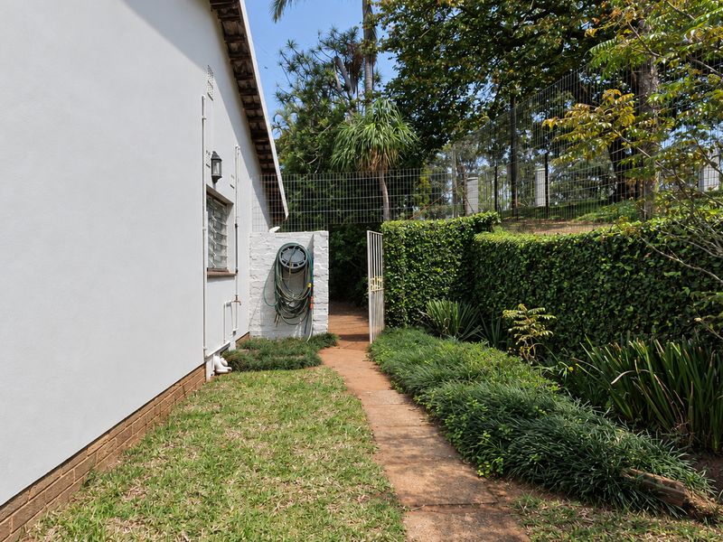 A well-maintained rear exterior area featuring a paved pathway, landscaped garden beds, and secure perimeter fencing along the side of the townhouse.