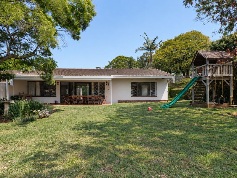 Spacious rear garden featuring a well-maintained lawn, mature trees, and a covered patio area attached to the main townhouse structure.