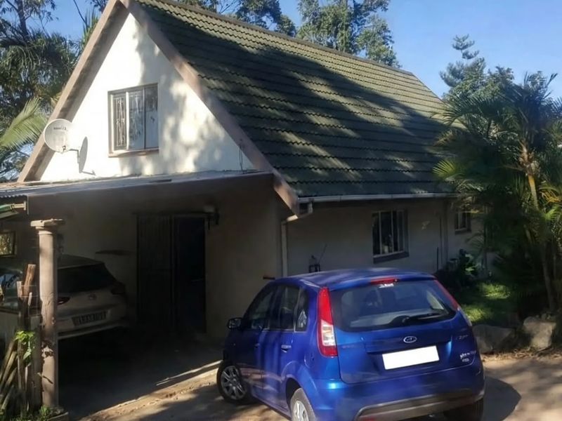 Front elevation of a townhouse featuring a pitched tiled roof, a covered carport area, and established garden surroundings.