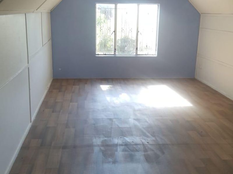 An empty bedroom featuring sloped ceilings, laminate flooring, and a window with security bars, offering a blank canvas for renovation.