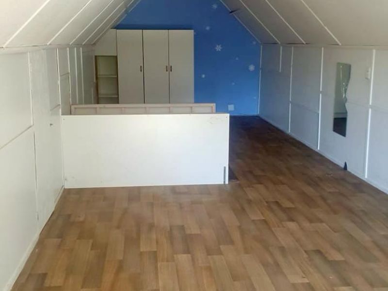 An attic-style bedroom featuring sloped ceilings, laminate flooring, and built-in storage cupboards, offering a versatile space for renovation or creative use.