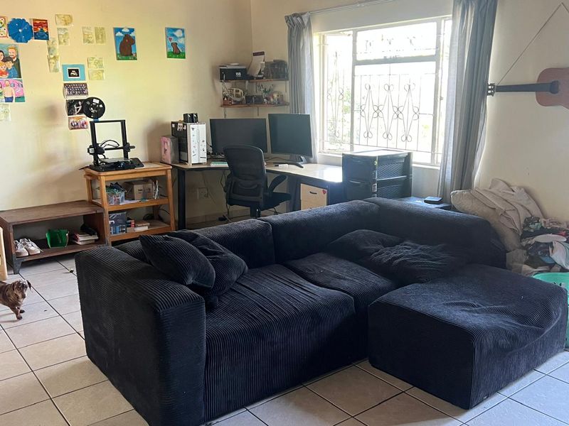 A living room area featuring tiled flooring and a window fitted with security bars, offering a functional space for relaxation or home office use.