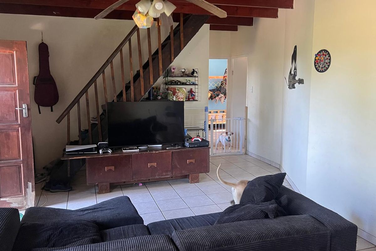 Living room featuring exposed timber ceiling beams, a timber staircase, and tiled flooring, offering a functional space with potential for cosmetic updates.