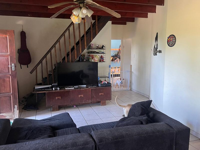 Living room featuring exposed timber ceiling beams, a timber staircase, and tiled flooring, offering a functional space with potential for cosmetic updates.