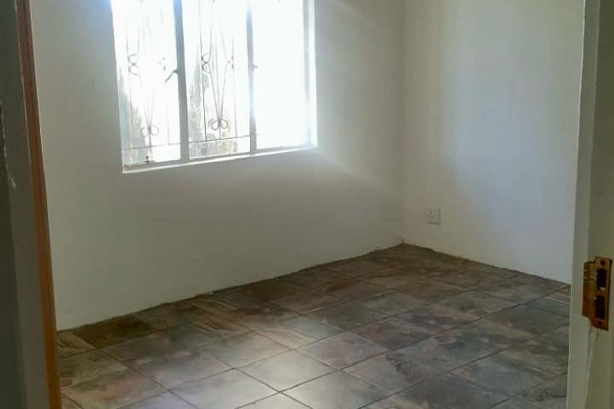 An empty bedroom featuring tiled flooring and a window with security bars, offering a blank canvas for potential interior design updates.