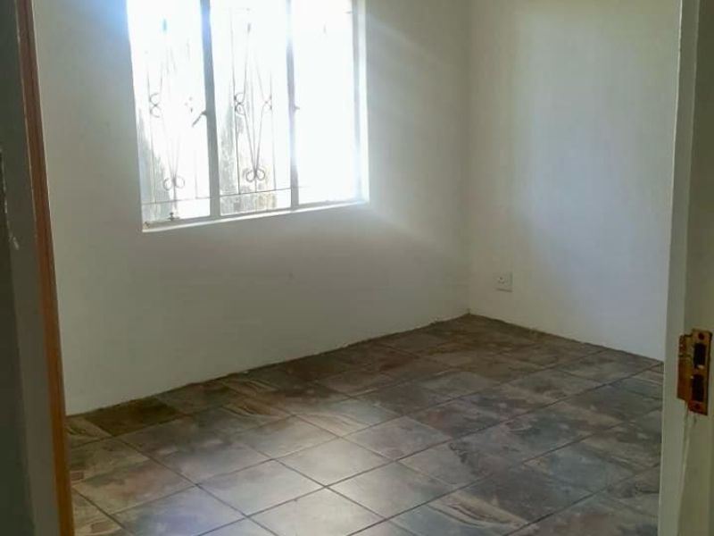 An empty bedroom featuring tiled flooring and a window with security bars, offering a blank canvas for potential interior design updates.