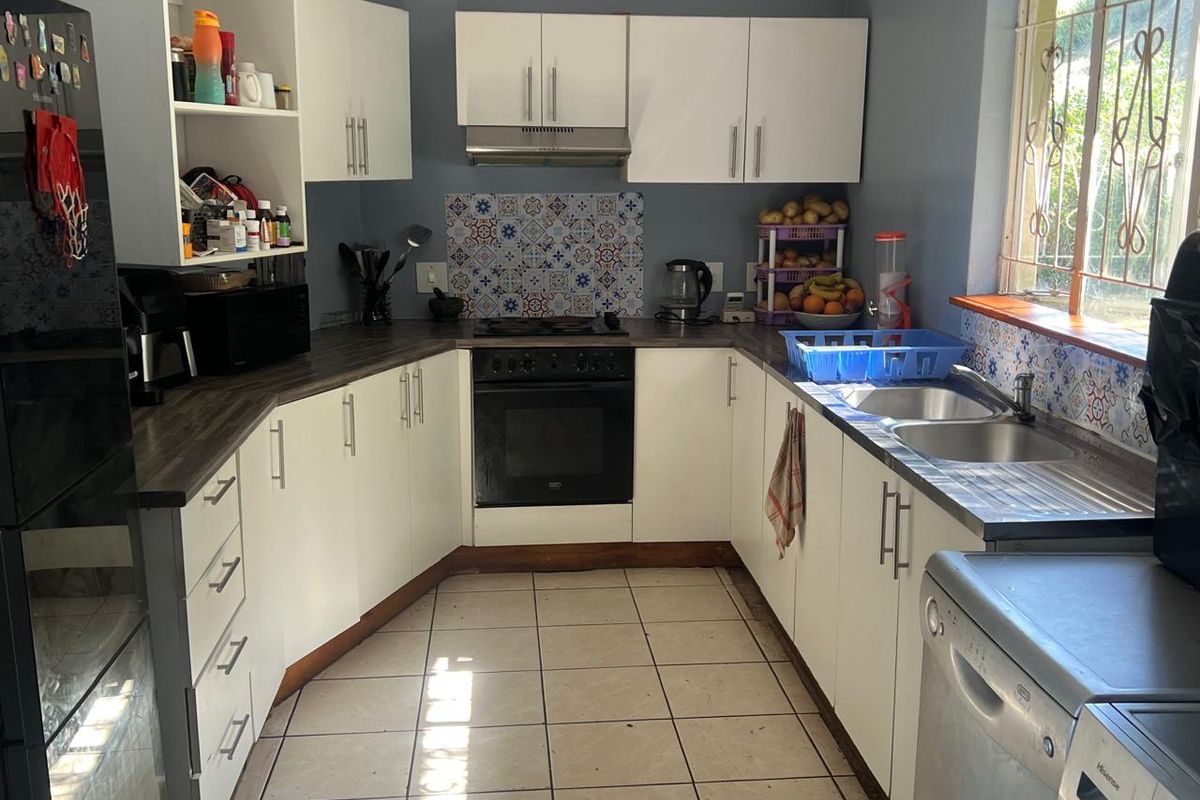 Functional kitchen featuring white cabinetry, dark laminate countertops, decorative tile backsplash, built-in oven, hob, extractor fan, and double sink with tiled flooring.