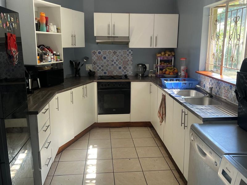 Functional kitchen featuring white cabinetry, dark laminate countertops, decorative tile backsplash, built-in oven, hob, extractor fan, and double sink with tiled flooring.