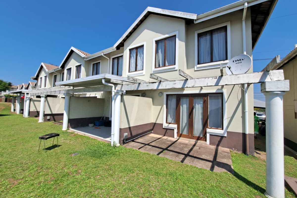 Rear view of a townhouse complex featuring a shared lawn, concrete patios, and wooden pergolas with integrated columns and sliding door access.