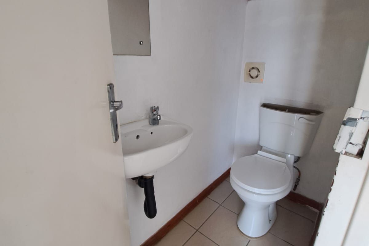 A small guest bathroom featuring a wall-mounted basin, toilet, and tiled flooring, currently requiring minor repairs and cosmetic updates.