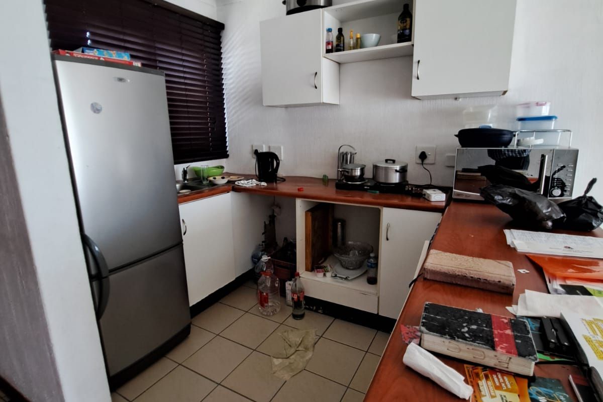 A compact kitchen featuring laminate countertops, white cabinetry, and ceramic floor tiles, currently requiring maintenance and repair to the lower cabinet section.