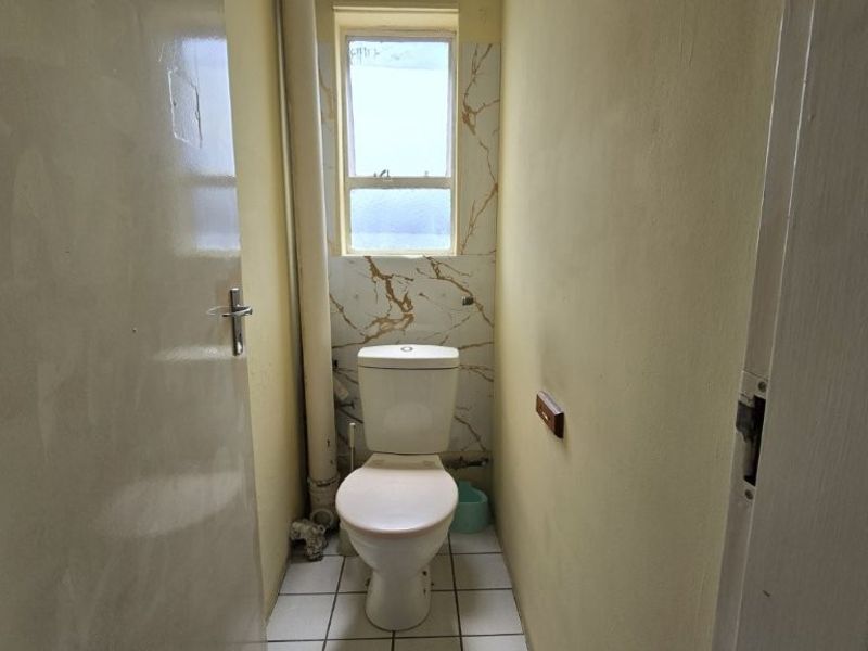 A compact, functional bathroom featuring a standard toilet, tiled flooring, and marble-effect wall accents around the window.