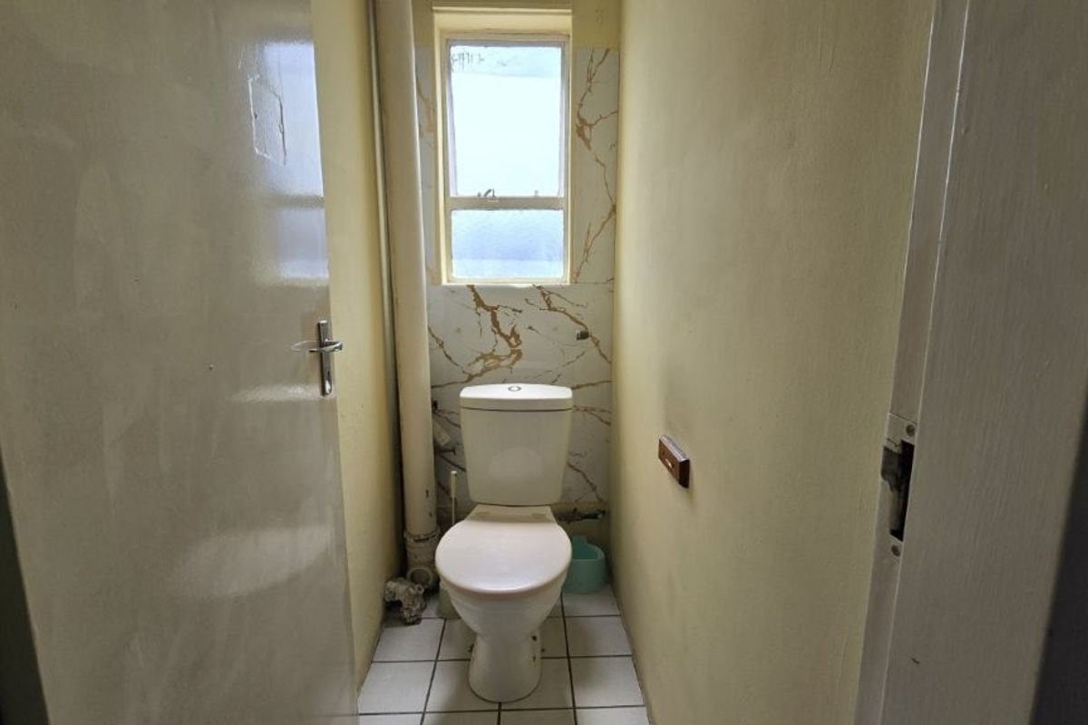 A compact, functional bathroom featuring a standard toilet, tiled flooring, and marble-effect wall accents around the window.