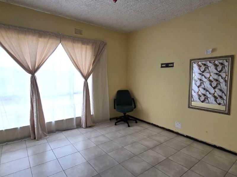 A spacious living area featuring tiled flooring and a large window, providing a blank canvas for potential interior design updates.