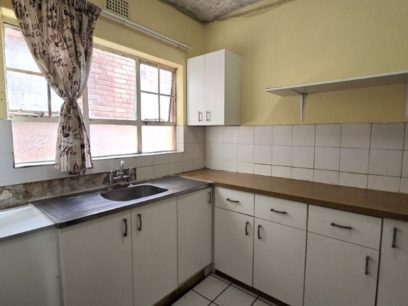A functional kitchen featuring laminate countertops, a stainless steel sink, tiled backsplash, and built-in cabinetry, requiring cosmetic updates to modernize the space.