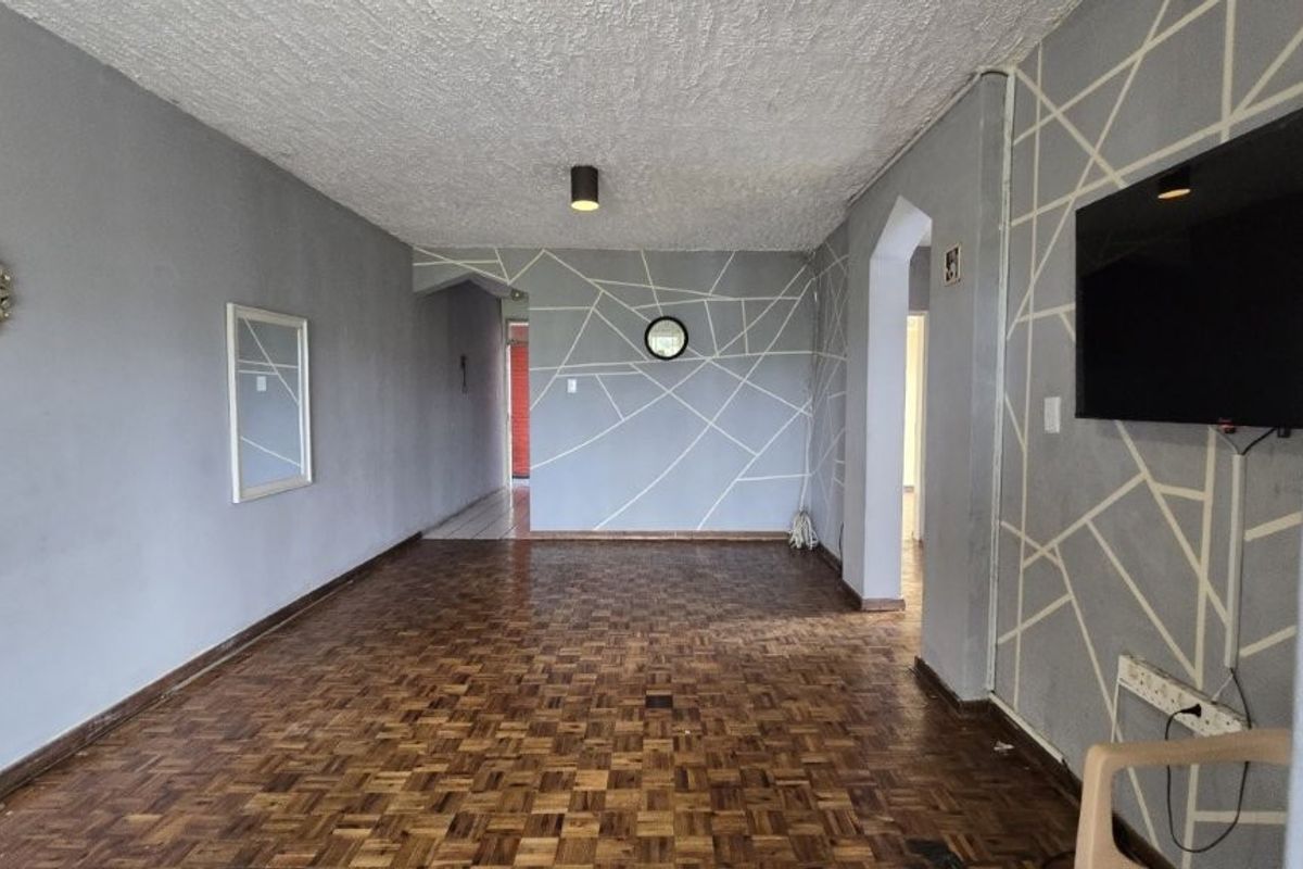 Spacious living area featuring traditional parquet flooring, textured ceiling, and decorative wall patterns, offering a blank canvas for renovation.