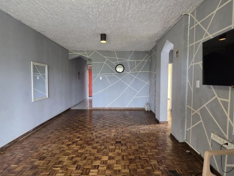 Spacious living area featuring traditional parquet flooring, textured ceiling, and decorative wall patterns, offering a blank canvas for renovation.