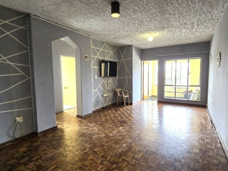 Spacious living area featuring traditional parquet flooring, a textured ceiling, and an archway leading to adjacent rooms, offering a blank canvas for renovation.