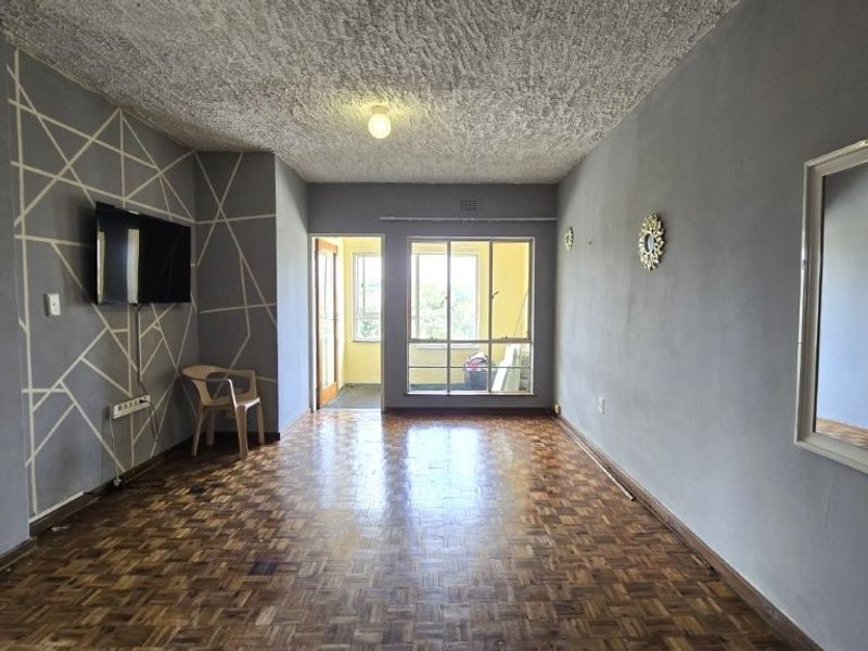 Spacious living area featuring traditional parquet flooring, textured ceiling, and large windows providing natural light and access to an adjoining balcony.