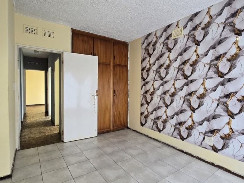 An empty bedroom featuring built-in wooden cupboards, tiled flooring, and a decorative feature wall, offering a blank canvas for renovation.
