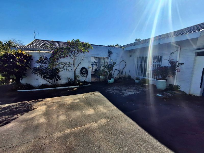 Rear exterior view of the property featuring a paved courtyard area, security gates, and white brick facade with security bars on windows.