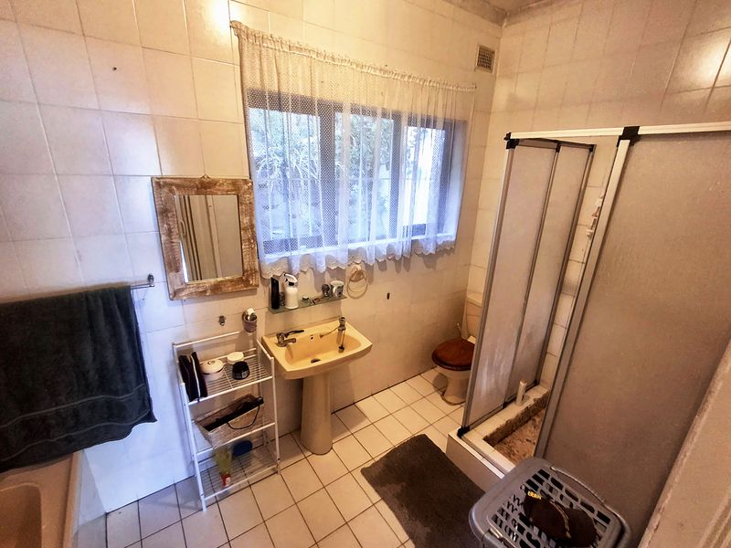 A dated bathroom featuring a pedestal basin, shower enclosure, and tiled finishes, offering significant potential for modernization and renovation.