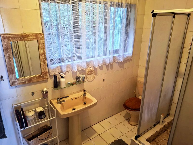A functional bathroom featuring a pedestal basin, toilet, and shower enclosure with tiled finishes throughout, offering potential for modernization.