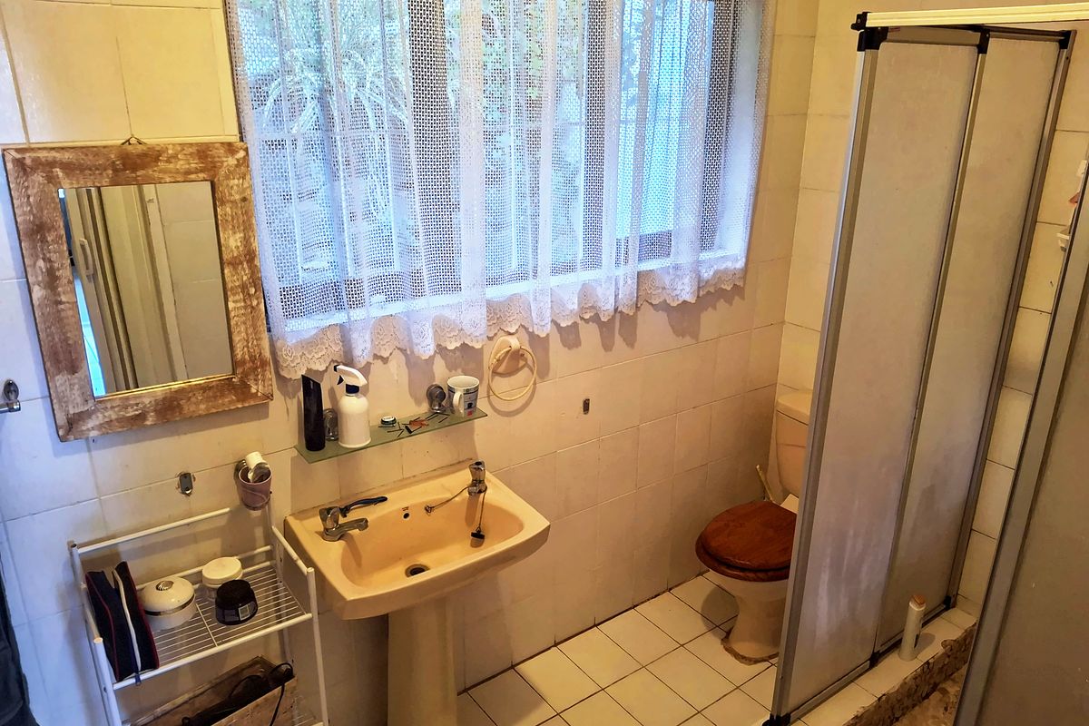 A functional bathroom featuring a pedestal basin, toilet, and shower enclosure with tiled finishes throughout, offering potential for modernization.