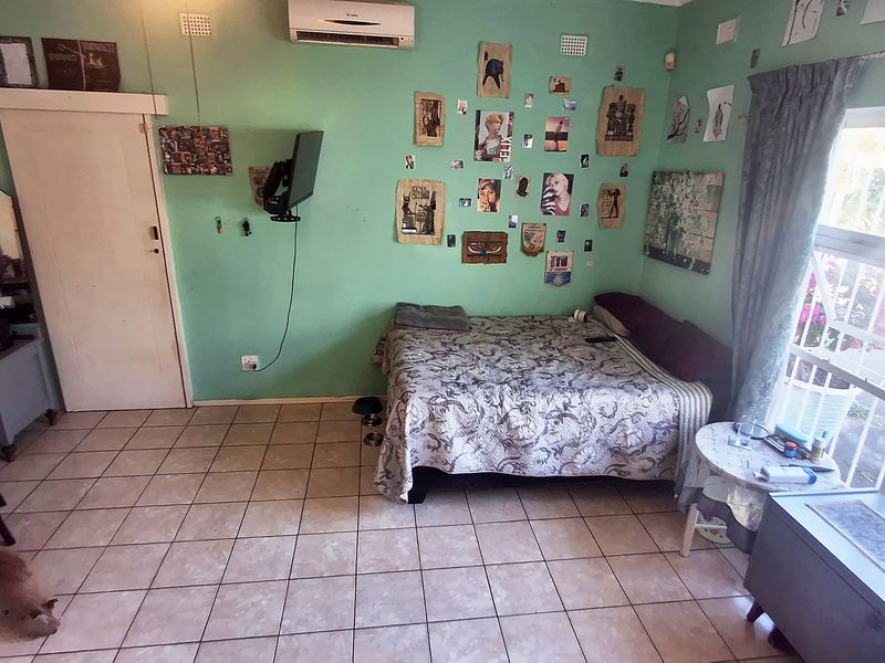A bedroom featuring tiled flooring, an air conditioning unit, and a large window, providing a functional space with potential for cosmetic updates.