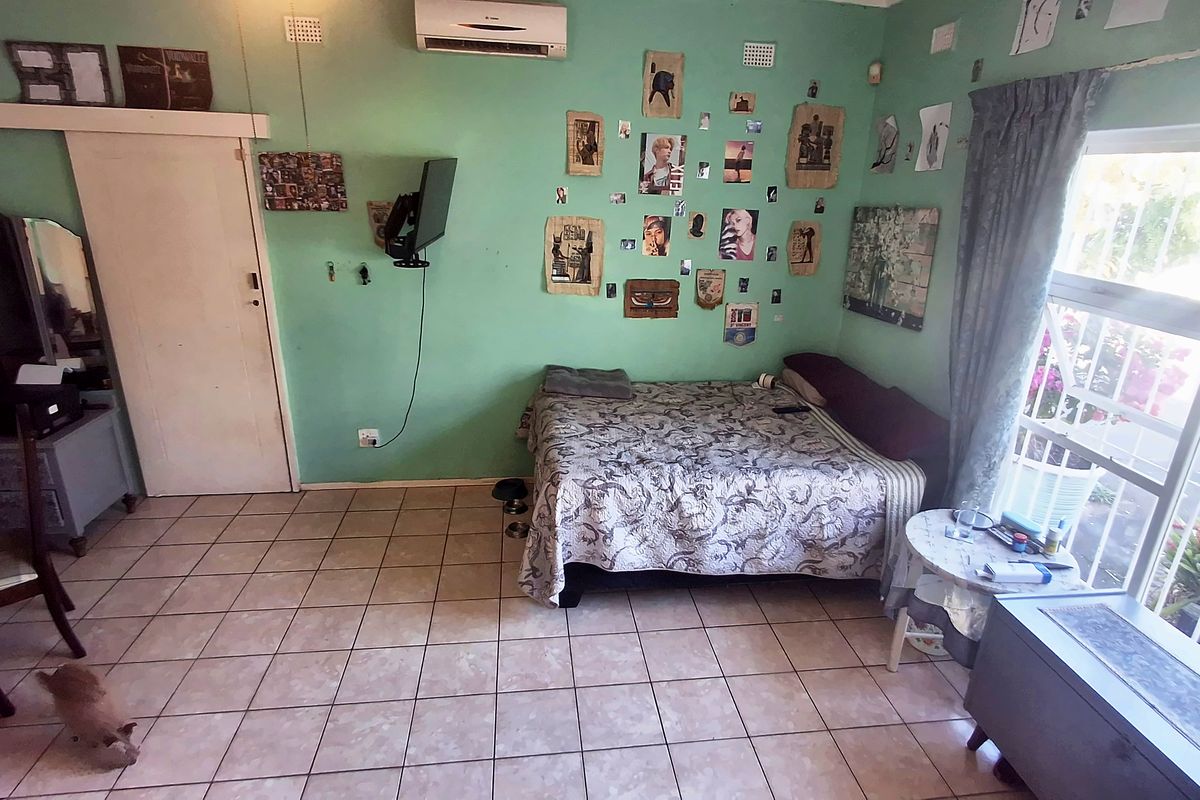 A bedroom featuring tiled flooring, an air conditioning unit, and a large window, providing a functional space with potential for cosmetic updates.