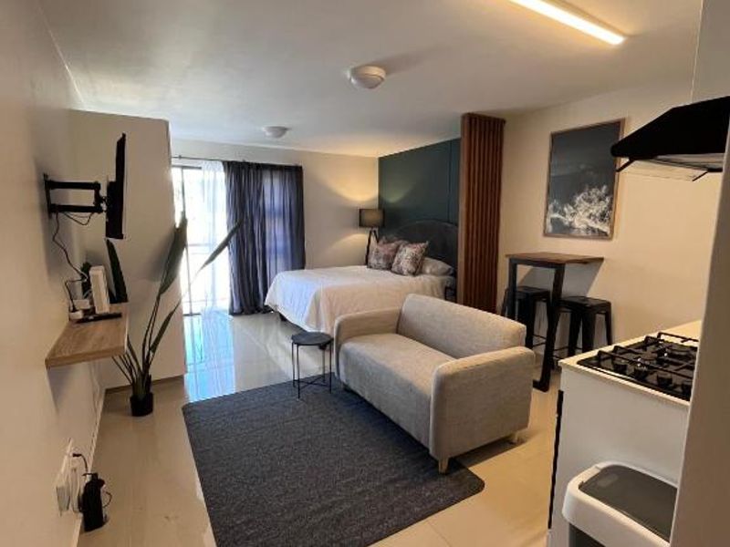 Open-plan studio apartment featuring a compact kitchen with gas hob, tiled flooring, and a combined living and sleeping area with access to a balcony.